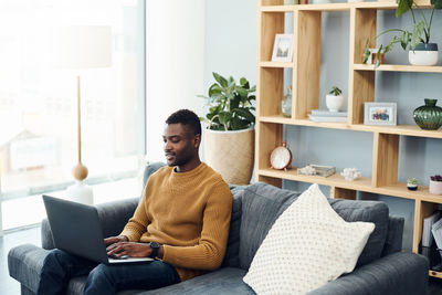 Young man using laptop while sitting on sofa at home