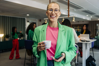 Portrait of happy female business professional holding coffee cup at office