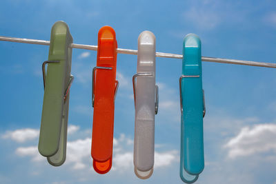 Low angle view of clothespins hanging against blue sky