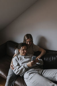 Female couple relaxing together on sofa and looking at cell phone