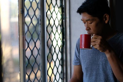 Mid adult man holding coffee cup in window