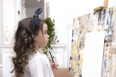 Dreamy pretty kid girl with paintbrush near drawing easel. little painting artist.