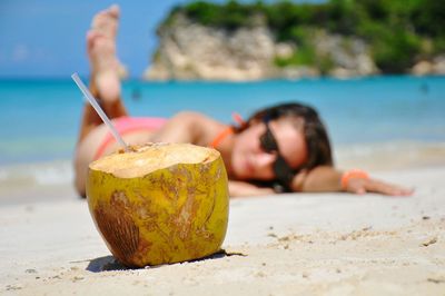 Woman lying at beach with coconut drink in foreground