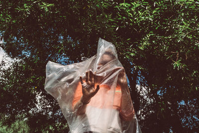Low angle view of woman wrapped in plastic while standing against trees