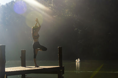 Mid adult woman in tree pose over pier