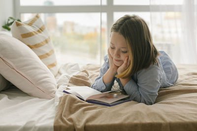 Young woman using mobile phone while sitting on bed at home