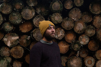 Male in winter clothes standing before a pile of logs freshly cut.