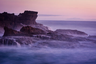 Rock formation in sea against sky during sunset