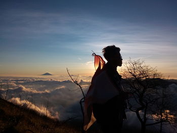 Side view of woman standing on mountain against sky during sunset