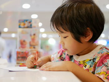 Cute girl coloring paper at table in restaurant