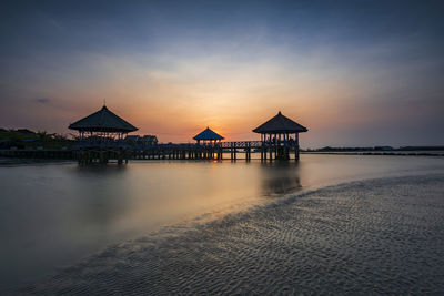 Built structure on beach against sky during sunset