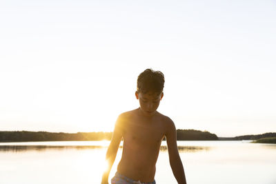 Shirtless boy looking down against clear sky on sunset