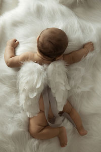 High angle view of cute baby boy wearing artificial wing while lying on fur blanket at home