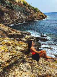 Woman sitting on rock by sea