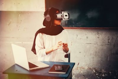 Woman using virtual reality simulator while sitting in classroom