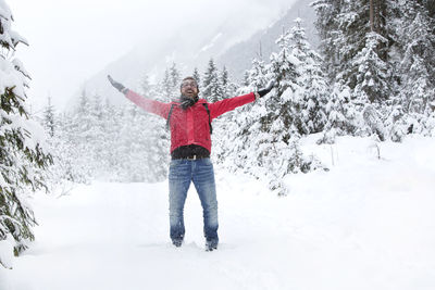 Happy young man with a red jacket and snow glasses throws up snow