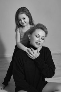 Mother in a black sweater hugs her five-year-old daughter sitting on a chair in the room in front