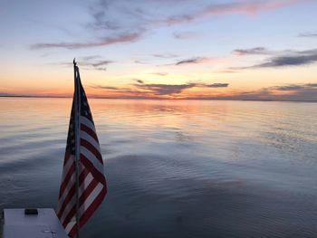 American flag with sea in background against sky during sunset