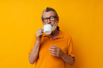 Young woman drinking milk against yellow background