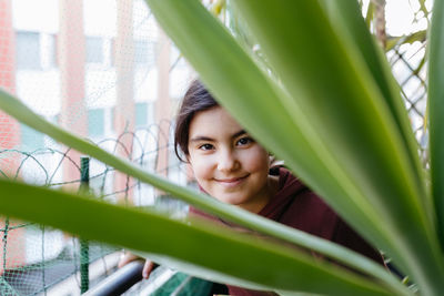 Portrait of girl with dark hair hiding behind the leaves of palm on the balcony