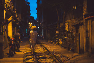 Rear view of people walking on illuminated street at night