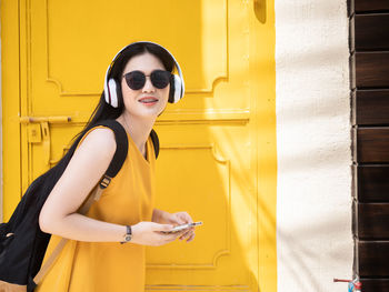 Young woman wearing sunglasses standing against yellow wall