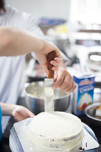 Cropped image of woman spreading cream on sponge cake at kitchen