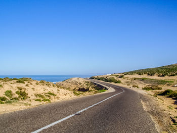 Road by sea against clear blue sky