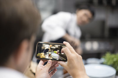 Chef photographing colleague preparing food in restaurant