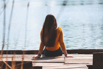 Rear view of woman sitting on pier over sea