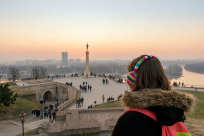 Rear view of woman looking at pobednik while listening music through headphones during sunset