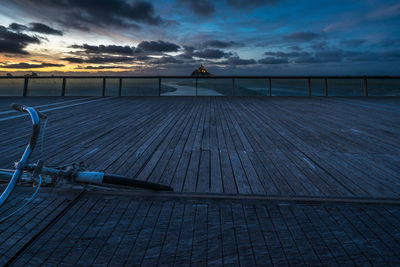 Bicycle on bridge against sky during sunset