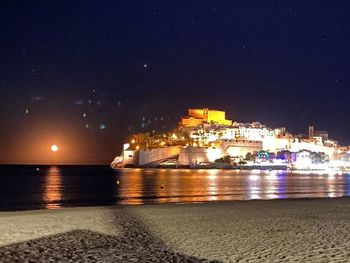 Illuminated city by sea against clear sky at night