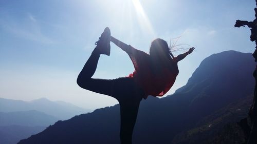 Rear view of woman performing yoga on mountain against sky