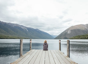 Woman on pier over lake against mountains