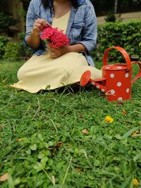 Midsection of woman holding red flowering plants on field