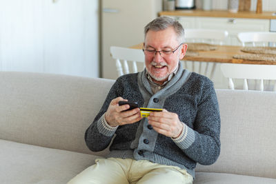 Young man using mobile phone while sitting on sofa at home