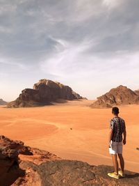 Rear view of man standing on rock against sky