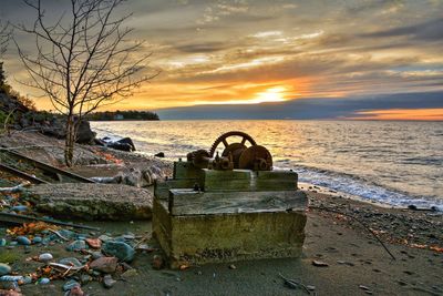 Abandoned boat on beach against sky during sunset