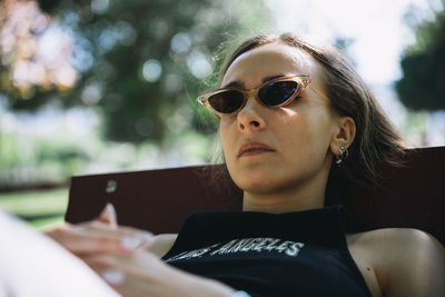 Portrait of young woman wearing sunglasses sitting on bench at park