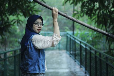 Side view portrait of woman standing on footbridge amidst trees