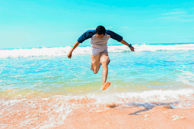 Young man jumping at beach against sky