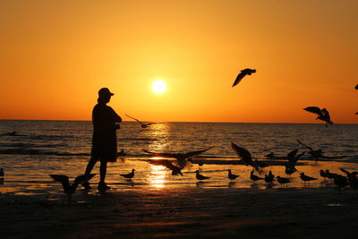 Silhouette people in sea against sky during sunset