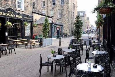 Empty chairs and tables in street amidst buildings in city