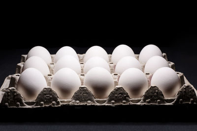 White chicken eggs in a cardboard box on black background
