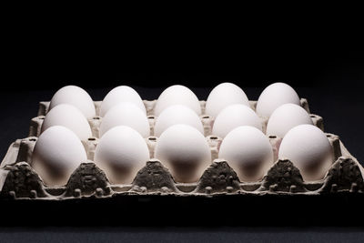 White chicken eggs in a cardboard box on black background