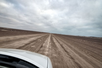 Car moving on road against cloudy sky