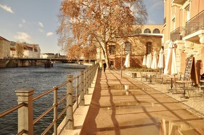 Footpath by river in city against sky