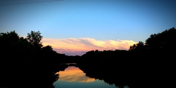 Silhouette trees by lake against sky during sunset