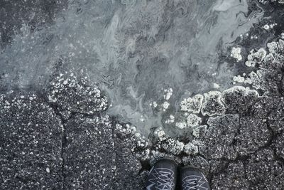 Low section of man standing at rocky sea shore